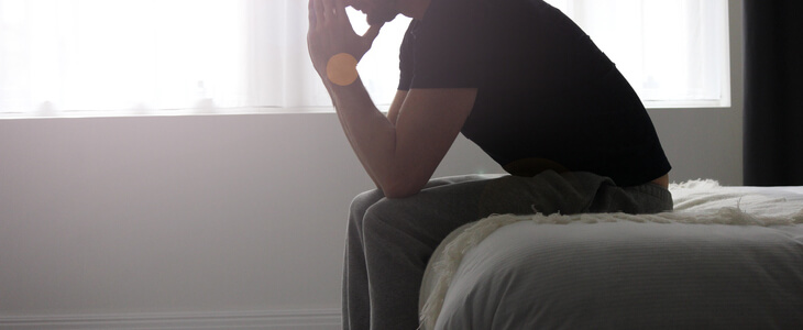Man sitting on his bed, visibly saddened